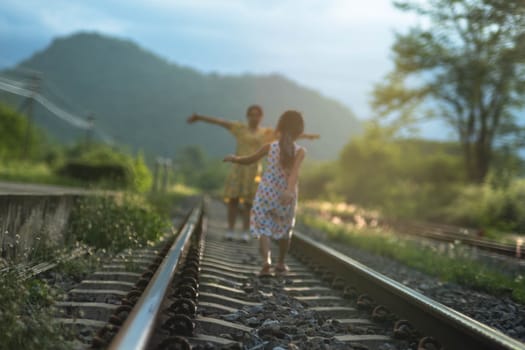 Mother and cute daughter walking on the railroad in the daytime. Happy family walking on the railway against the background of mountains and greenery.