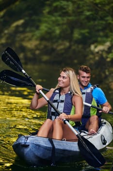 A young couple enjoying an idyllic kayak ride in the middle of a beautiful river surrounded by forest greenery.