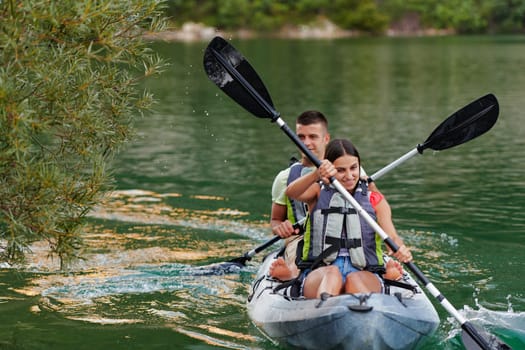 A young couple enjoying an idyllic kayak ride in the middle of a beautiful river surrounded by forest greenery.