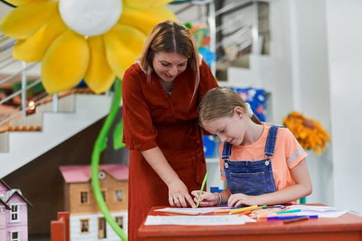 Creative kids during an art class in a daycare center or elementary school classroom drawing with female teacher. High quality photo