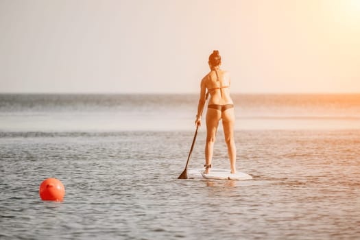 Sea woman sup. Silhouette of happy middle aged woman in rainbow bikini, surfing on SUP board, confident paddling through water surface. Idyllic sunset. Active lifestyle at sea or river