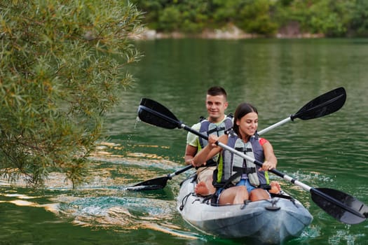 A young couple enjoying an idyllic kayak ride in the middle of a beautiful river surrounded by forest greenery.