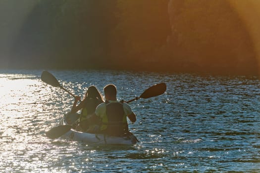 A young couple enjoying an idyllic kayak ride in the middle of a beautiful river surrounded by forest greenery in sunset time.