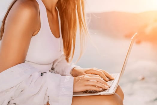 Digital nomad, Business woman working on laptop by the sea. Pretty lady typing on computer by the sea at sunset, makes a business transaction online from a distance. Freelance remote work on vacation