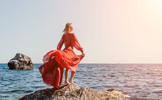 Woman travel sea. Young Happy woman in a long red dress posing on a beach near the sea on background of volcanic rocks, like in Iceland, sharing travel adventure journey