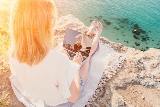 Woman sea laptop. Business woman in yellow hat working on laptop by sea. Close up on hands of pretty lady typing on computer outdoors summer day. Freelance, digital nomad, travel and holidays concept.