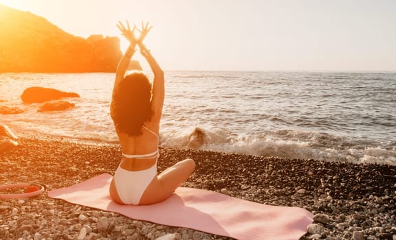 Young woman in swimsuit with long hair practicing stretching outdoors on yoga mat by the sea on a sunny day. Women's yoga fitness pilates routine. Healthy lifestyle, harmony and meditation concept.