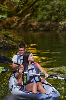 A young couple enjoying an idyllic kayak ride in the middle of a beautiful river surrounded by forest greenery.