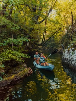 A young couple enjoying an idyllic kayak ride in the middle of a beautiful river surrounded by forest greenery.