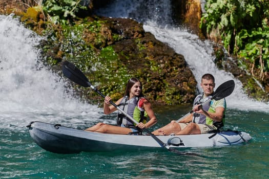 A young couple enjoying an idyllic kayak ride in the middle of a beautiful river surrounded by forest greenery.