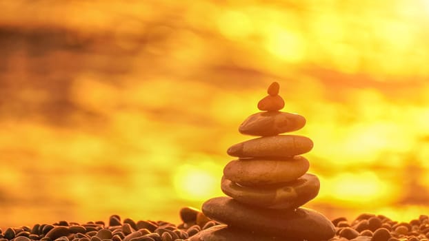 Balanced rock pyramid on pebbles beach. Golden sea bokeh on background. Selective focus, zen stones on sea beach, meditation, spa, harmony, calm, balance concept