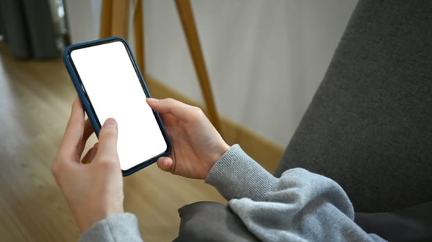 Closeup view of woman hands holding smartphone, lying on couch at home. White screen for advertising text.