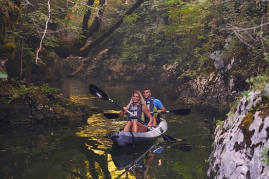 A young couple enjoying an idyllic kayak ride in the middle of a beautiful river surrounded by forest greenery.