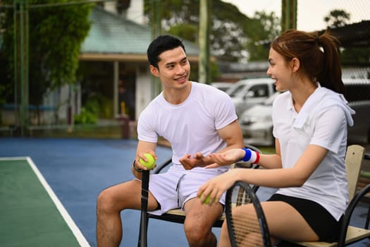 Male and female tennis players talking and resting after game. Sport activity, tennis training and competition concept.