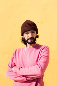 stylish young man smiling looking at camera with arms crossed in a yellow background, concept of youth and modern lifestyle, copy space for text
