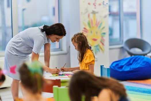 Creative kids during an art class in a daycare center or elementary school classroom drawing with female teacher