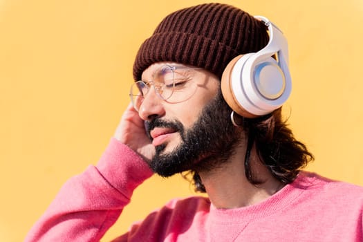 young man listening to music on headphones with yellow background, concept of rhythm and positive people, copy space for text