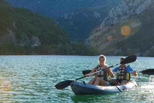 A young couple enjoying an idyllic kayak ride in the middle of a beautiful river surrounded by forest greenery in sunset time.