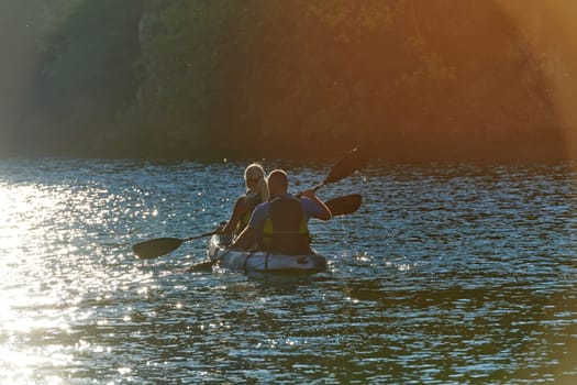 A young couple enjoying an idyllic kayak ride in the middle of a beautiful river surrounded by forest greenery in sunset time.