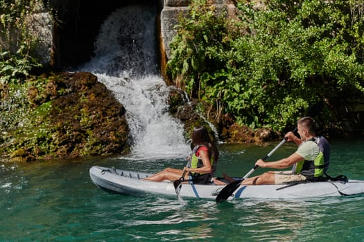 A young couple enjoying an idyllic kayak ride in the middle of a beautiful river surrounded by forest greenery.