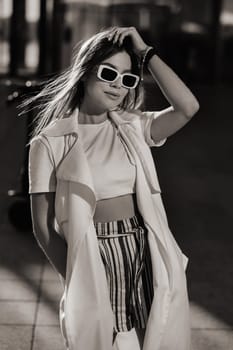 Stylish girl in glasses and a white summer coat in the city.