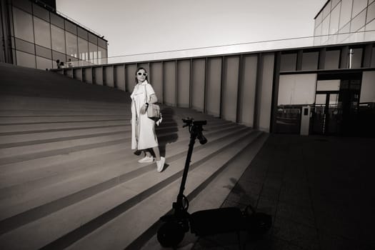 Stylish girl in glasses and a white summer coat in the city with a handbag.