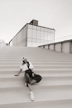 A young teenage girl in jeans and a cap is sitting on the stairs in the city.