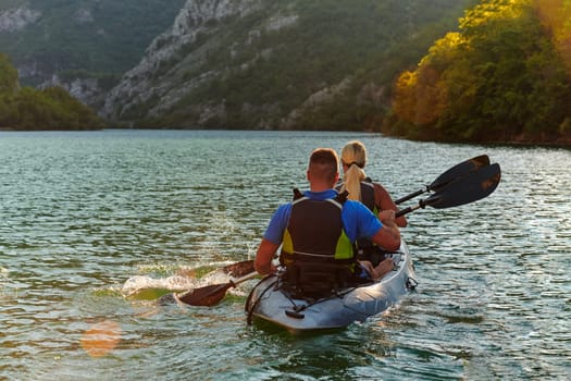 A young couple enjoying an idyllic kayak ride in the middle of a beautiful river surrounded by forest greenery in sunset time.