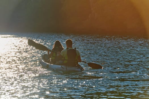 A young couple enjoying an idyllic kayak ride in the middle of a beautiful river surrounded by forest greenery in sunset time.