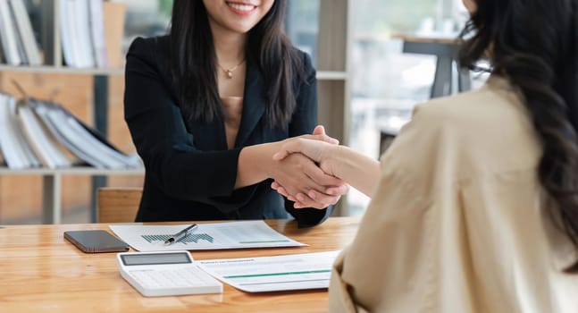 businesspeople shake hand after their partnerships in conference room and finalized pile of papers of financial report and data analysis on meeting table.