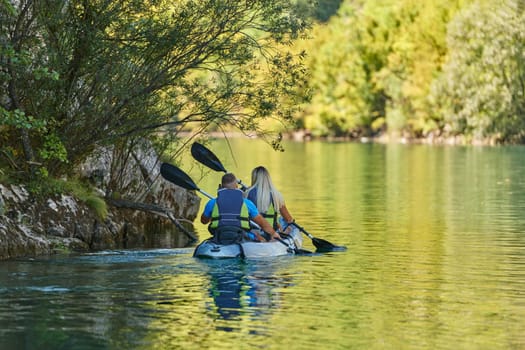 A young couple enjoying an idyllic kayak ride in the middle of a beautiful river surrounded by forest greenery.