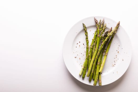 Overhead view of asparagus and seasoning in plate by copy space against white background. unaltered, food, healthy eating and organic concept.