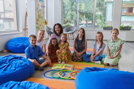 A happy female teacher sitting and playing hand games with a group of little schoolchildren.