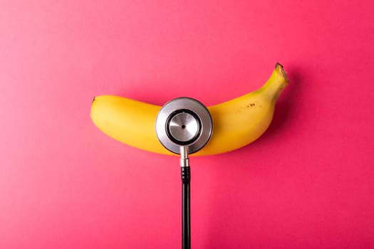 Directly above view of fresh banana with stethoscope by copy space over pink background. unaltered, organic food, healthy eating and medical equipment concept.