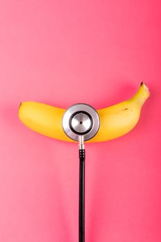 Overhead view of fresh banana with stethoscope by copy space on pink background. unaltered, organic food, healthy eating and medical equipment concept.