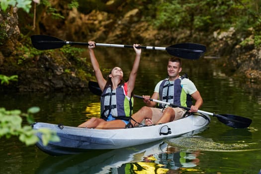 A young couple enjoying an idyllic kayak ride in the middle of a beautiful river surrounded by forest greenery.