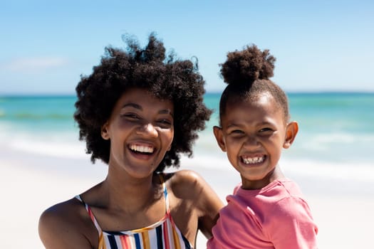 Portrait of happy african american mother and daughter enjoying sunny day at beach. unaltered, family, lifestyle, togetherness, enjoyment and holiday concept.