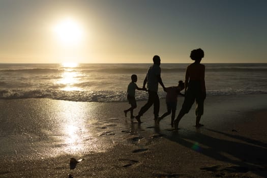 Full length of african american family holding hands walking at beach during sunset. unaltered, family, lifestyle, togetherness, enjoyment and holiday concept.