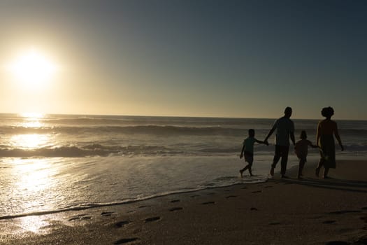 African american family walking while holding hands at beach with copy space during sunset. unaltered, family, lifestyle, togetherness, enjoyment and holiday concept.