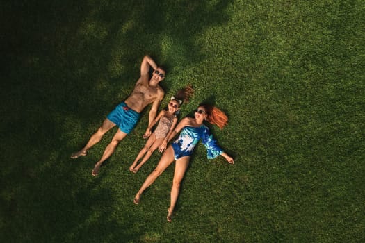 Top view of a happy family in swimsuits lying on the green grass.