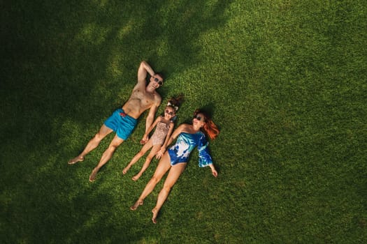 Top view of a happy family in swimsuits lying on the green grass.