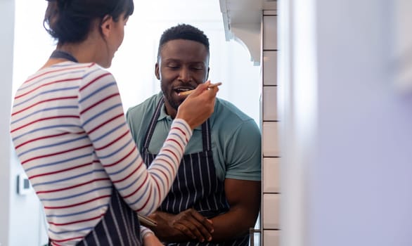 Caucasian young woman feeding food to african american boyfriend at home. unaltered, lifestyle, togetherness, preparing food, love, domestic life, food.