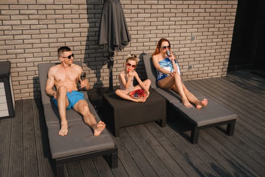 A happy family in swimsuits sunbathe in summer on their terrace on sun beds.