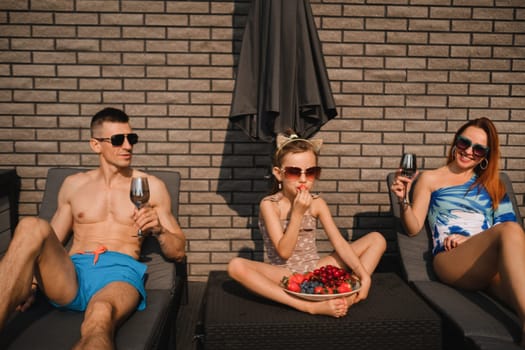 A happy family in swimsuits sunbathe in summer on their terrace on sun beds.