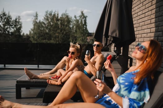 A happy family in swimsuits sunbathe in summer on their terrace on sun beds.