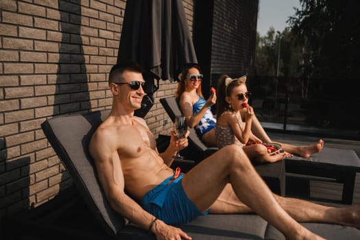 A happy family in swimsuits sunbathe in summer on their terrace on sun beds.