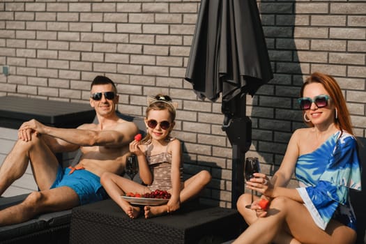 A happy family in swimsuits sunbathe in summer on their terrace on sun beds.