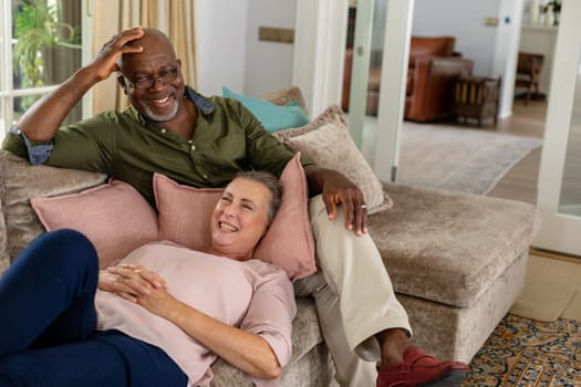Happy senior multiracial couple spending leisure time together on sofa at home. unaltered, lifestyle, retirement, togetherness, leisure.