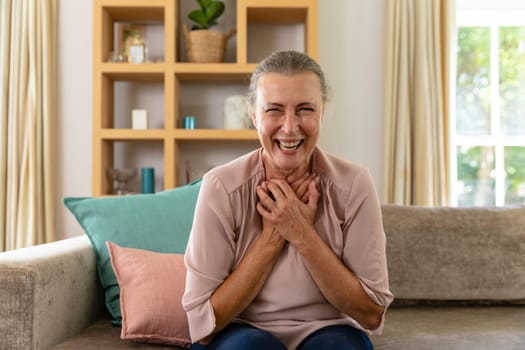 Portrait of happy caucasian senior woman sitting on sofa at home. unaltered, lifestyle, retirement, leisure, happiness, domestic life.