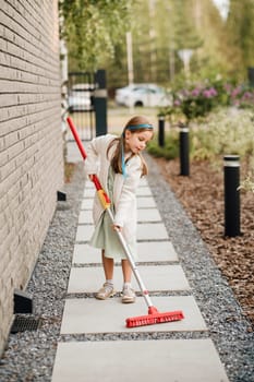 A little girl with a brush cleans a path on the street in the courtyard.